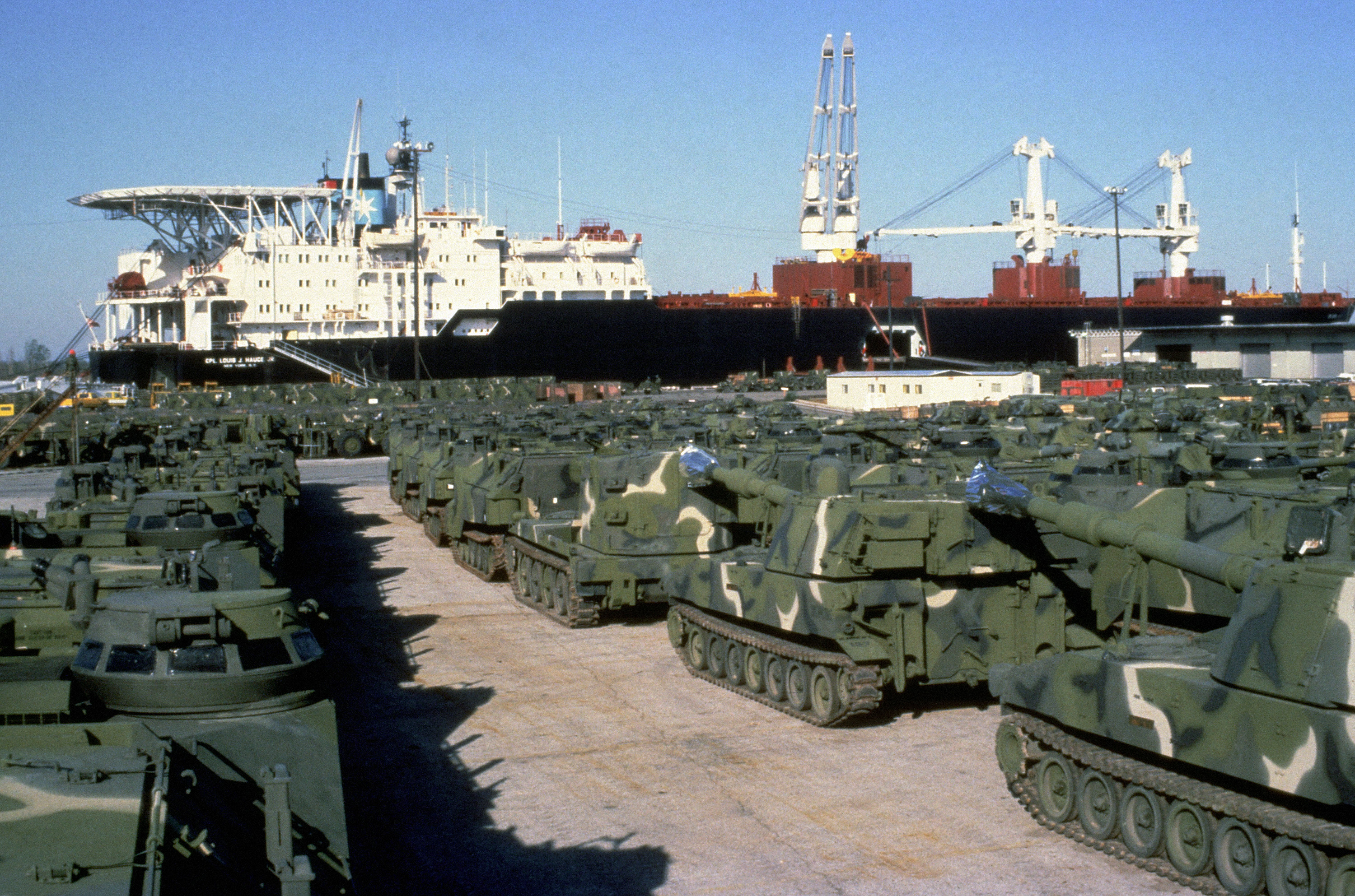 Personnel tracked landing vehicles, (LVTP7) and M109A2 155 mm self-propelled howitzers are staged on the wharf prior to being loaded aboard the Maersk class maritime prepositioning ship SS CPL. LOUIS J. HAUGE JR. The ship is being loaded with equipment of the 6th Marine Amphibious Brigade.Kilde: US national archives, public domain.